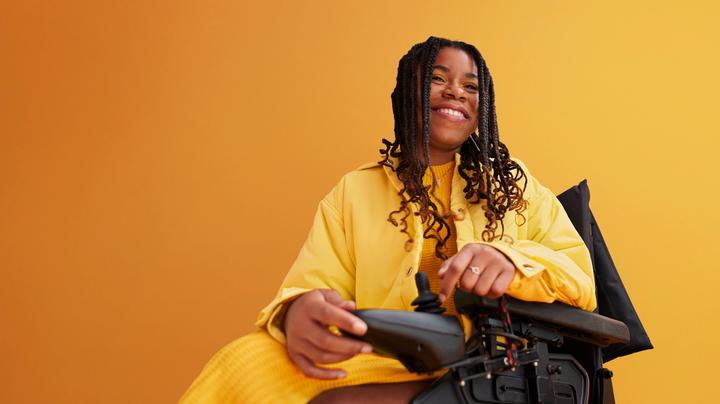 Smiling woman in a wheelchair, wearing a yellow top in front of a yellow background