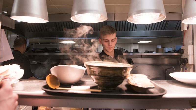 A chef working in a kitchen with a tray of steaming dishes in the foreground