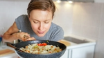 Женщина вдыхает аромат от сковороды с рисом и овощами