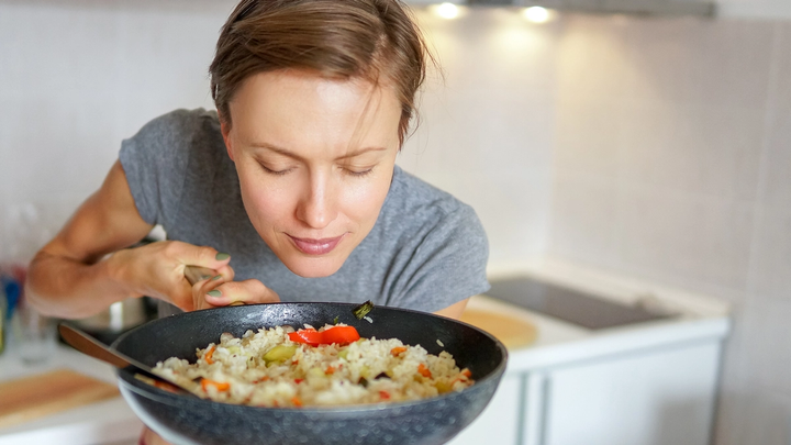 Una mujer saboreando el aroma de una sartén con arroz y verduras