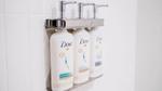 Bottles of Dove shampoo, conditioner and body wash in silver pump dispensers on a white tiled bathroom wall.