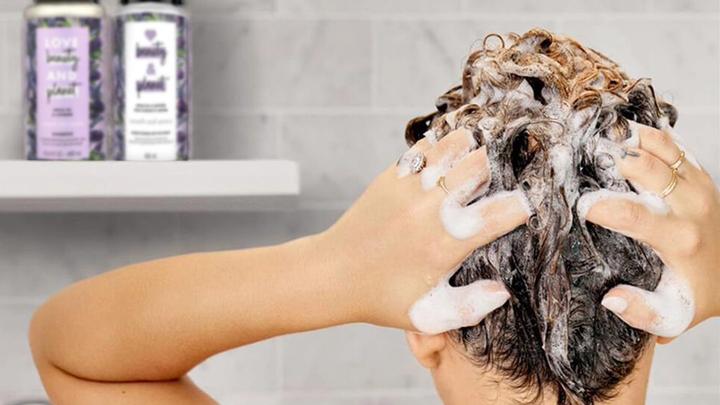 The back of a women’s head as she washes her hair. Love Beauty & Planet bottle sit on the shelf in front of her