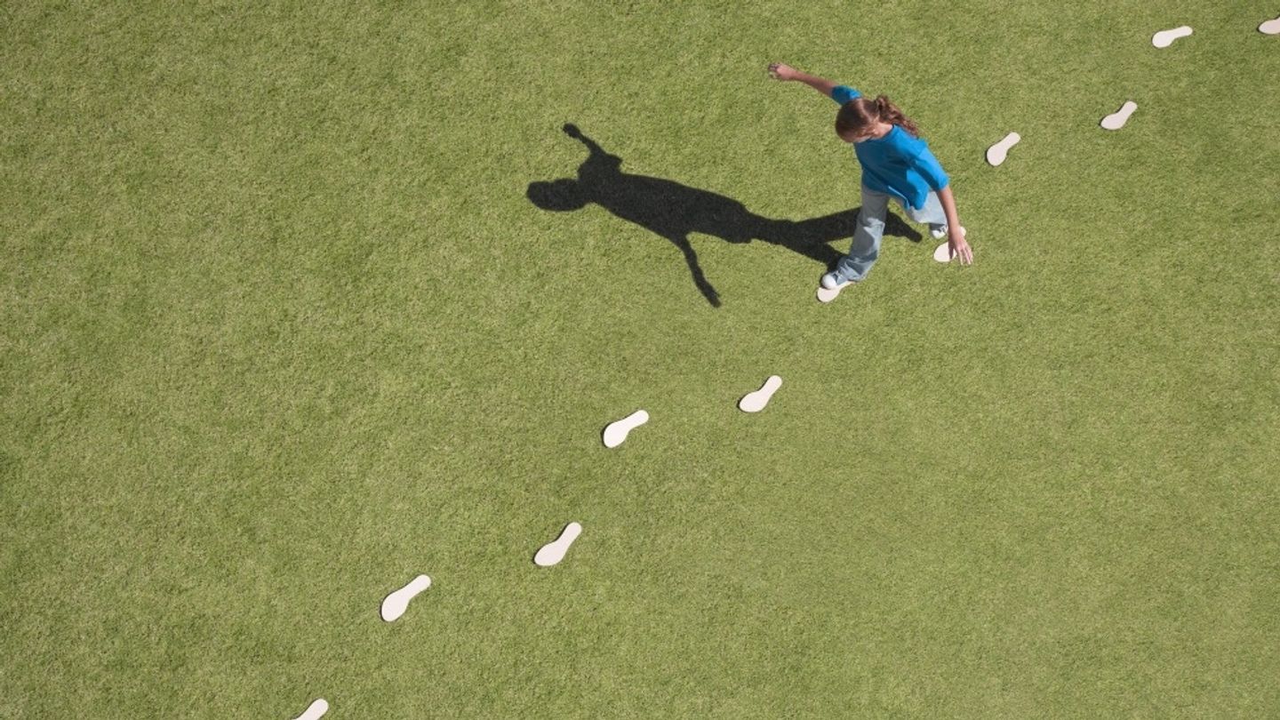A woman walks on white footprints across a grassy field