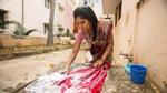 Jeune femme de l’Asie du Sud-est lavant des vêtements en tissus à l’eau savonneuse, à l’extérieur