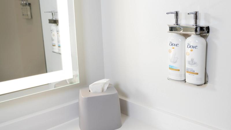 Bottles of Dove shampoo, conditioner and body wash in silver pump dispensers on a white tiled bathroom wall.