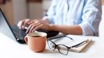 a close up of hands at a laptop with a pair of glasses and a cup of coffee in the foreground