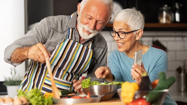 A man and woman preparing food in a kitchen from a recipe on a phone