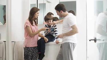 Mutter, Vater und Kind im Badezimmer, die Signal auf die Zahnbürsten auftragen. 