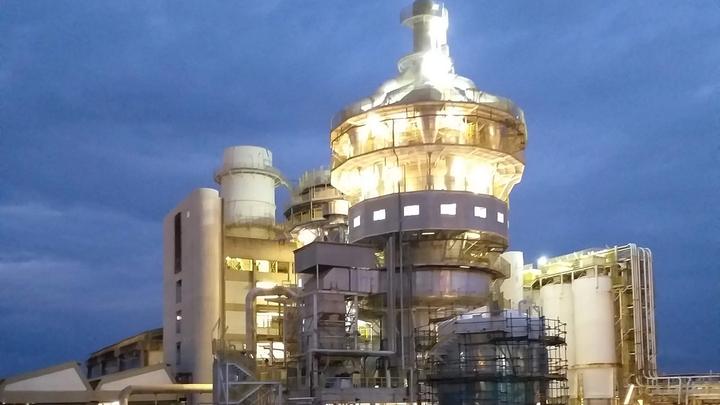 An illuminated factory tower against a dark blue night sky