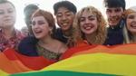Young diverse people having fun holding LGBT rainbow flag outside