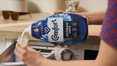 Person pouring Comfort fabric conditioner into bottle cap ready to put in washing machine.