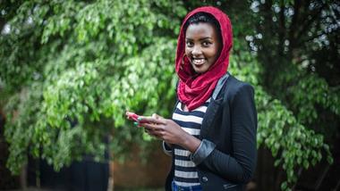 Woman holding mobile phone to make use of the Kasha mobile e-commerce platform in Rwanda