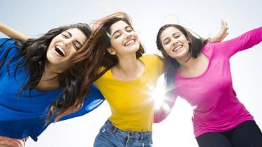 Beautiful girls in bright colored shirts of pink, blue, and yellow and having fun in the sun. Their long hair flowing in the air