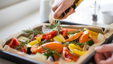 A person pouring olive oil over a roasting pan full of vegetables