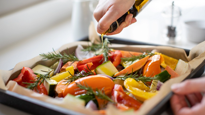 A person pouring olive oil over a roasting pan full of vegetables
