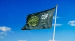 A green flag bearing the logo for COP 28 flutters in a clear blue sky.