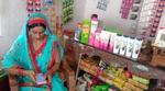 Indian woman store owner using mobile phone app while sitting next to shelves of consumer products.
