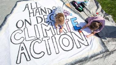 Two girls colouring in an 'All hands on deck climate action' poster