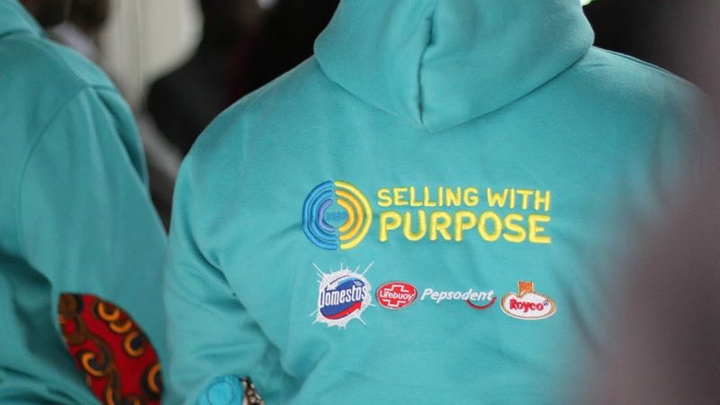 close up of a jacket that has the slogan 'selling with purpose' and a number of Unilever brand logos beneath it