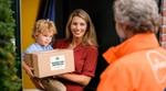 A smiling woman holds her child as she stands at her front door and accepts a parcel from Too Good To Go.