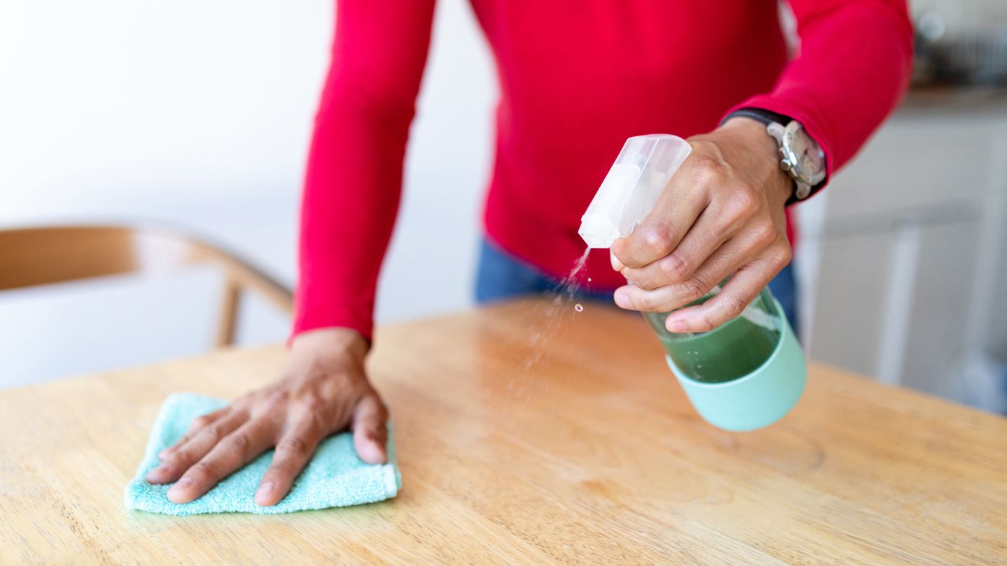 Person using spray bottle and cloth to wipe wooden tabletop. Unilever has developed a fully recyclable spray bottle.