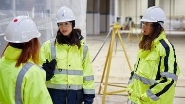 Three women in hard hats and high visibility jackets discuss a construction project at our factory in Turkey