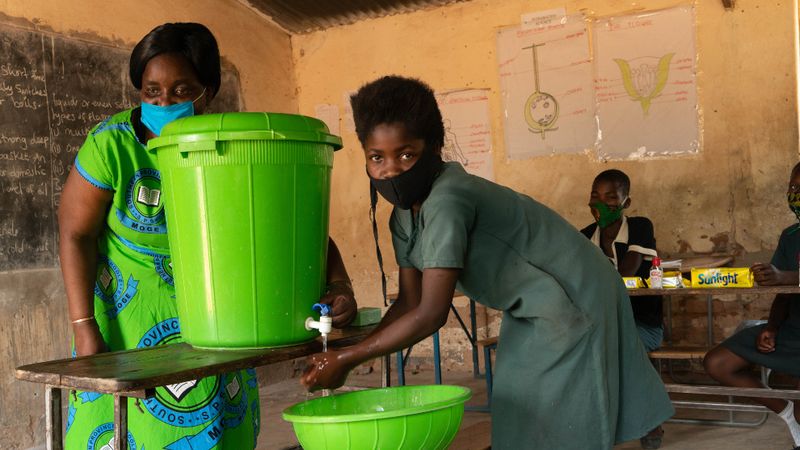 A green hand washing station is used by two women