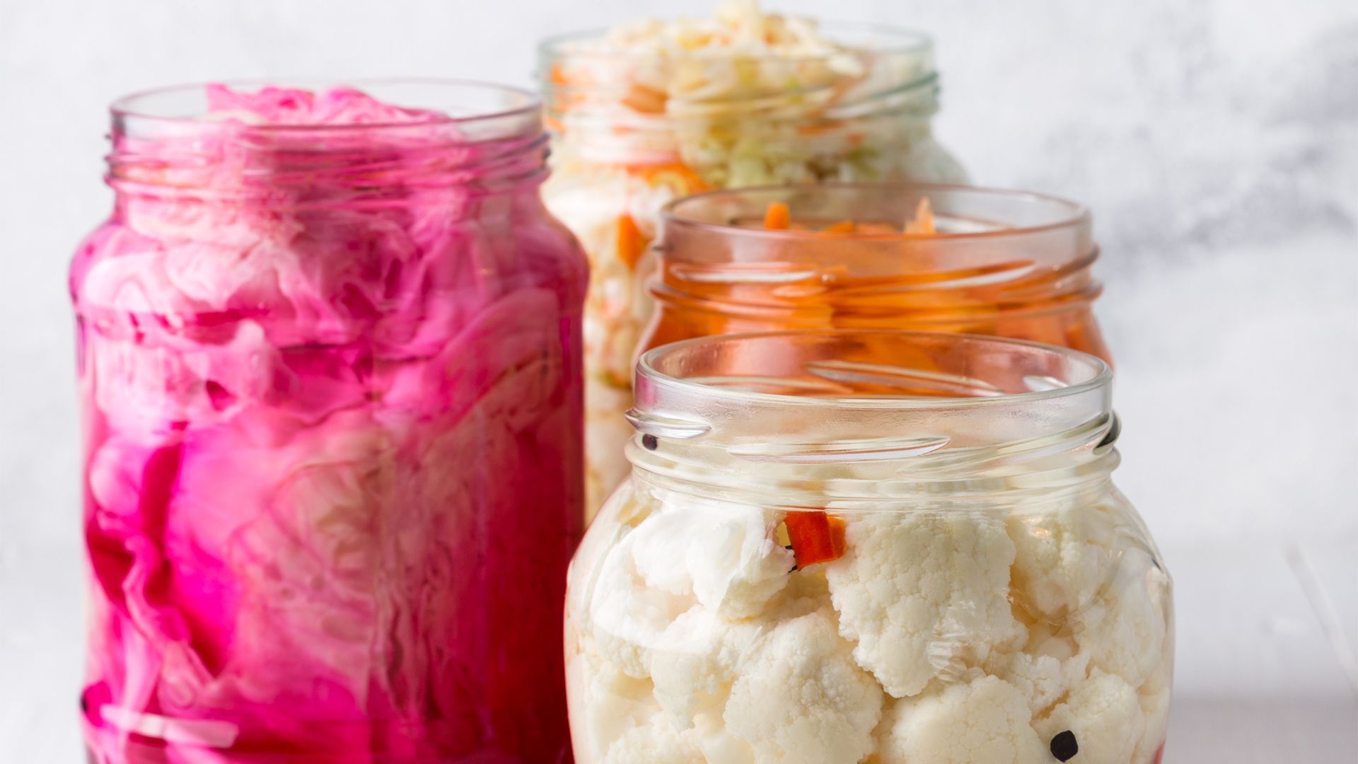 Three jars of fermented vegetables including sauerkraut and kimchi