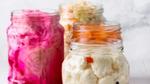 Three jars of fermented vegetables including sauerkraut and kimchi