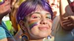 Someone smiling among a group of people with a rainbow-painted face and rainbow earrings.