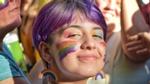 Someone smiling among a group of people with a rainbow-painted face and rainbow earrings.