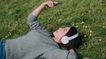 Young woman wearing headphones and studying phone, relaxes on a grassy field