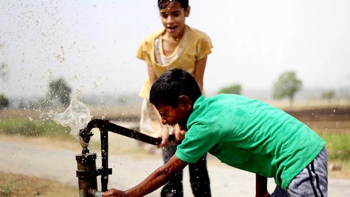 Two boys drinking and splashing water from a community water tap