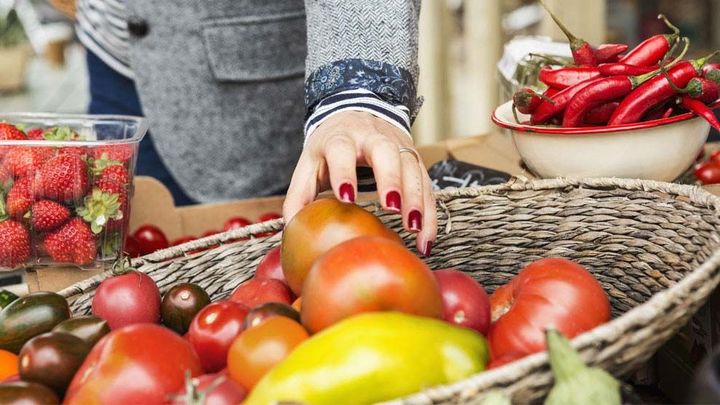 A womans hand reaching into a basket of vegetables