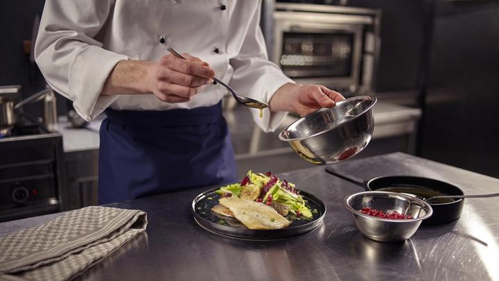 Chef in a commercial kitchen preparing a dish using a Knorr product.