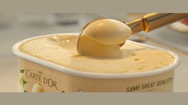 A scoop of ice cream being taken from a tub of Carte D'Or Vanilla