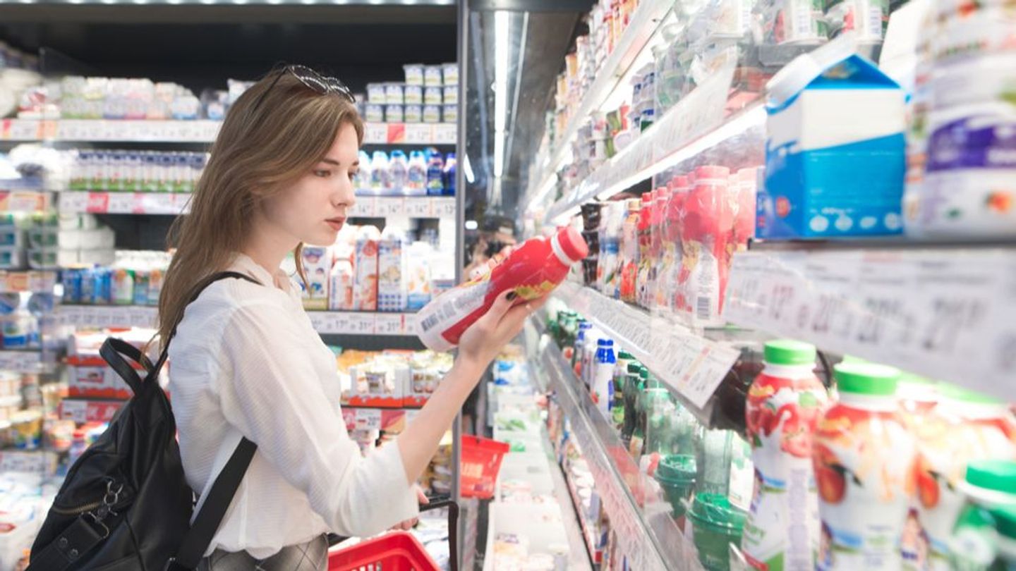 Woman in grocery store, holding a product and looking at its label.