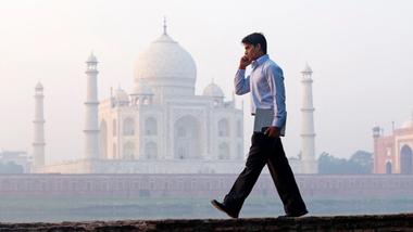 Man on the phone walking along a bridge in front of the Taj Mahal