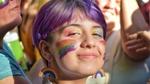 Smiling young woman with purple hair and pride rainbow face paint and earrings