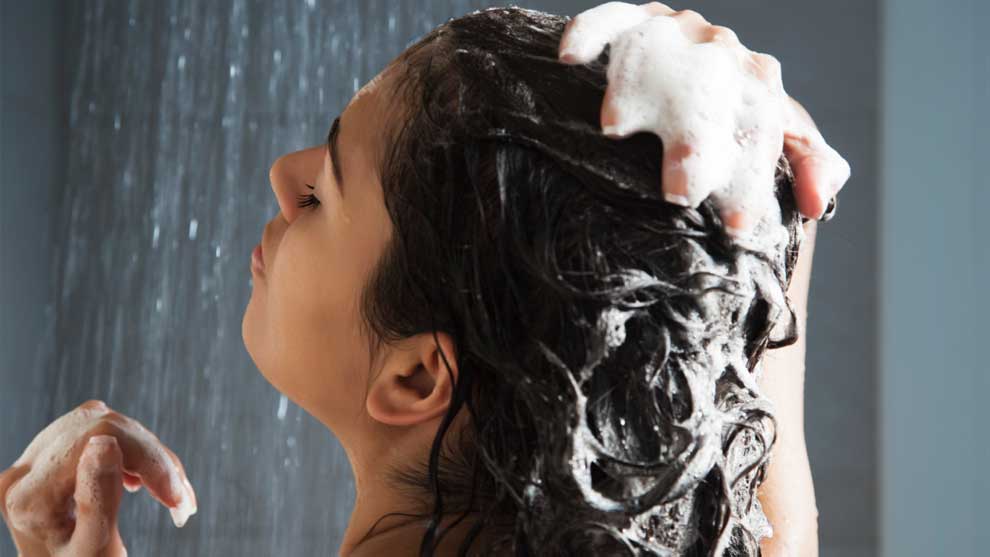 Žena koja šamponira kosu pod tušem