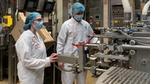 Man and women in hairnets and white coats on a factory floor checking machinery