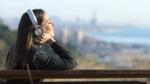 A woman with headphones sitting on bench overlooking a city in the distance