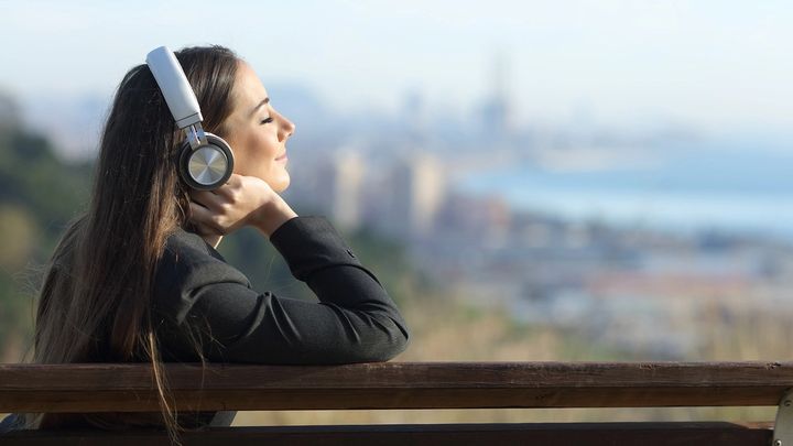 A woman with headphones sitting on bench overlooking a city in the distance