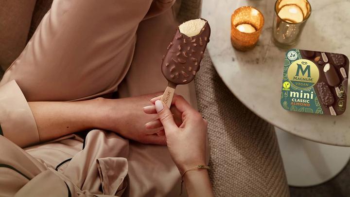 Woman sitting beside a table with a multi-pack of vegan Mini Magnums and holding a vegan Mini Magnum in her hand