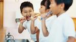 Three smiling children brushing teeth