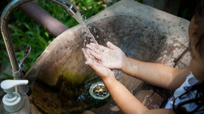 A young girl washes her hands with liquid soap at an outdoor sink