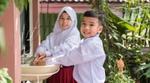Two smiling Indonesian schoolchildren wash their hands at an outdoor sink.