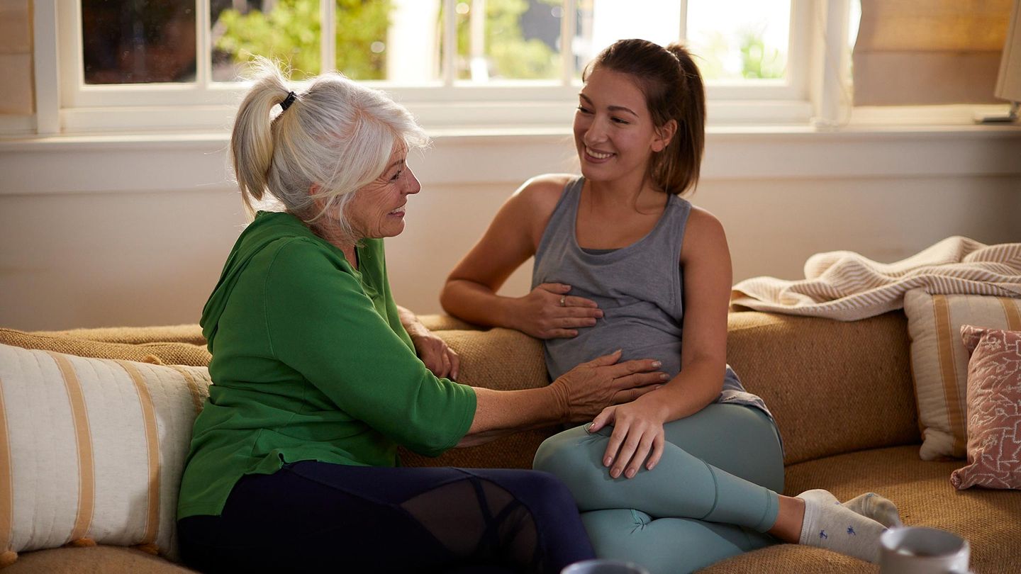 Two women sitting on the couch. One feeling the pregnant woman's tummy