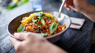 Hand holding a bowl of chickpeas and vegetables with mint