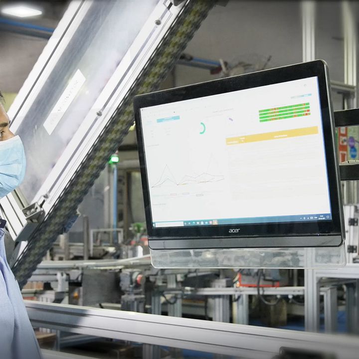 Man in front of two computer screens with a factory setting blurred in the background